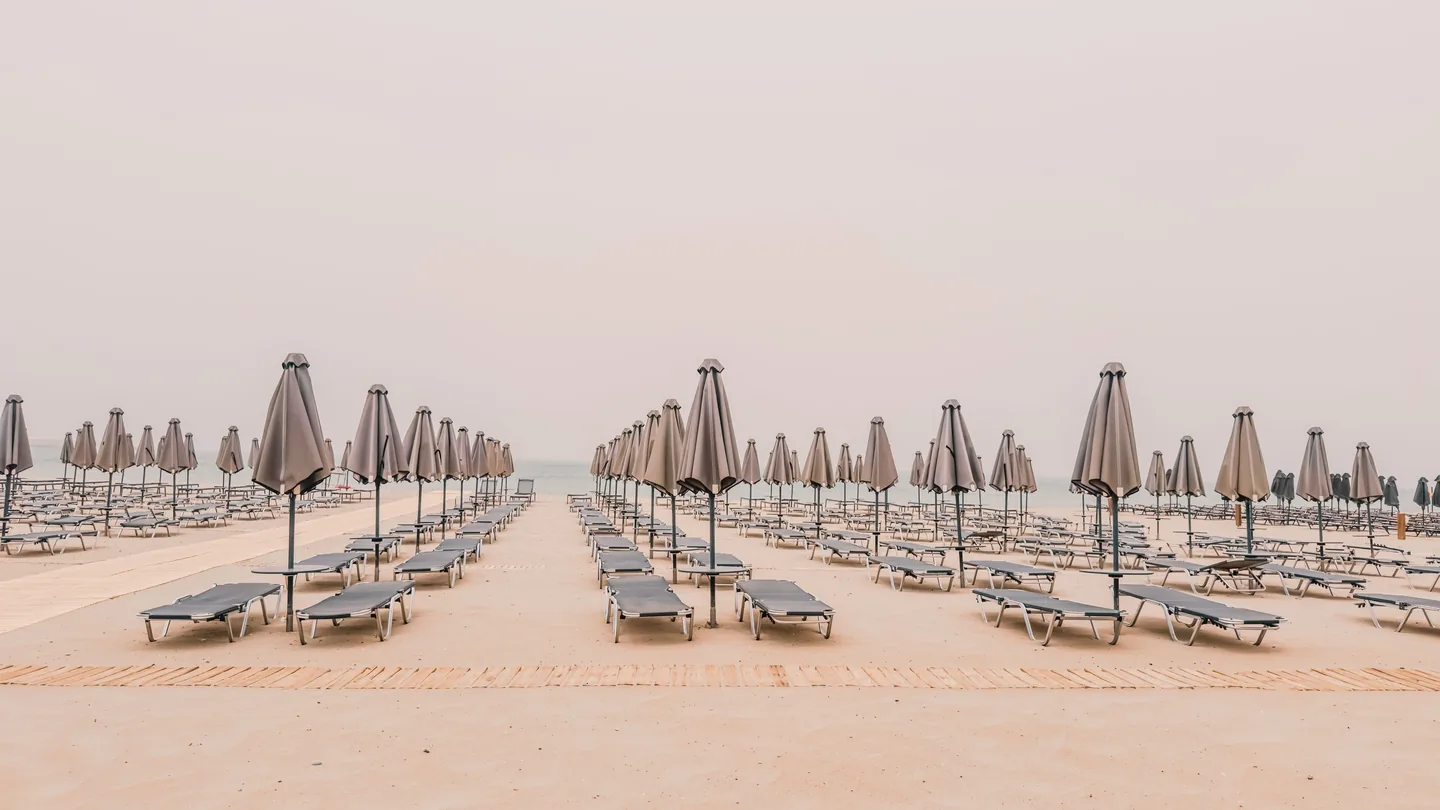 Rows of empty sun loungers and closed parasols on a wide sandy beach at Rethymno, Crete, early in the day